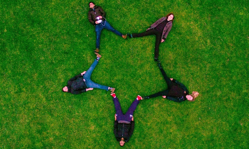 creating Company culture part 2. five employees laying in a field with their feet touching to form a star.